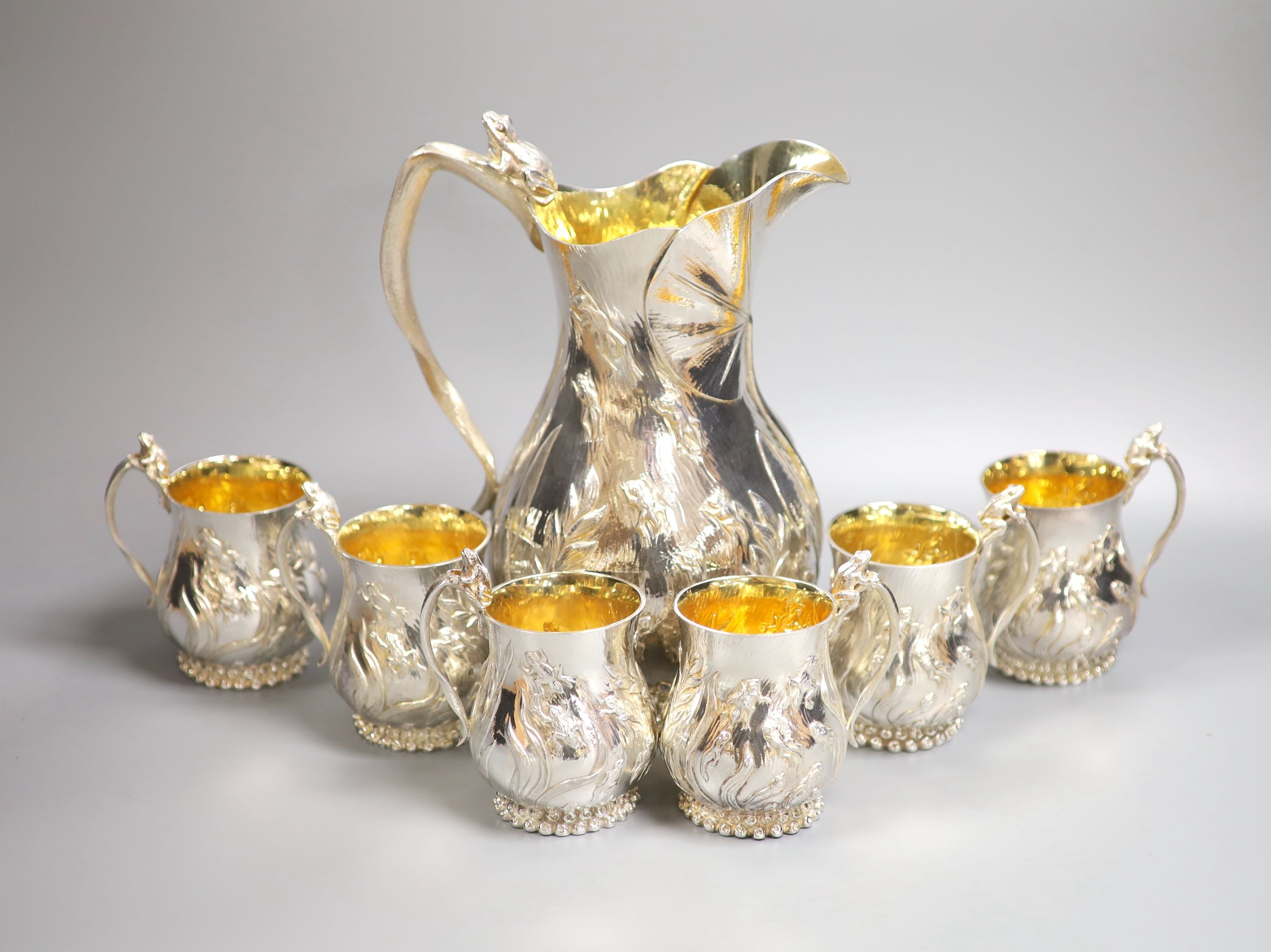 A good set of six Garrard & Co Ltd silver mugs and a matching jug, London, 1997, all embossed with frogs spawn amongst reeds, with gilded interiors, jug height 27.1cm